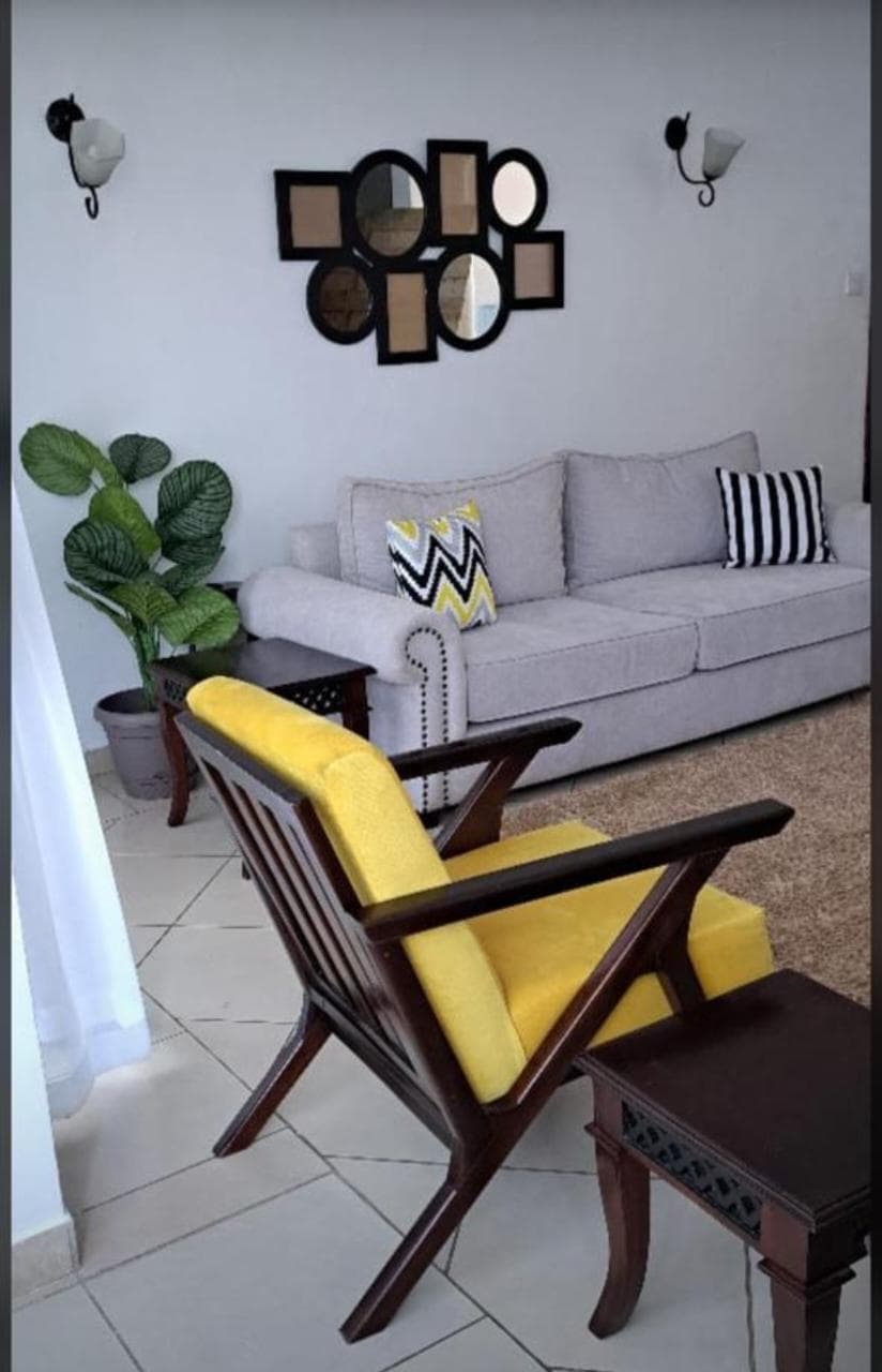 Light-grey three-seater photographed with a yellow wooden-arm chair.